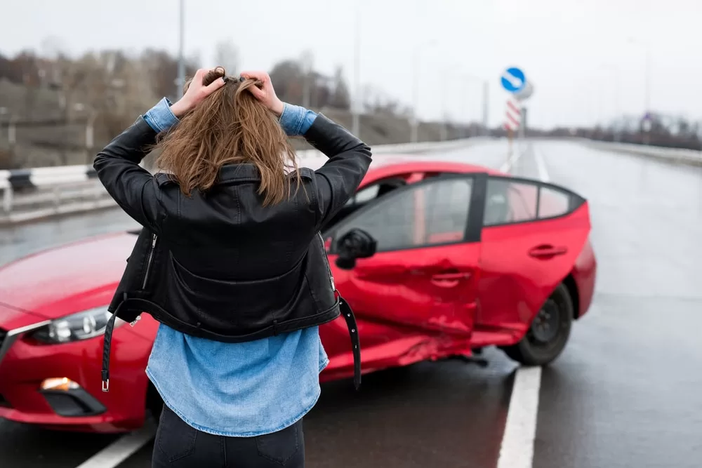 Woman in distress looking at her crashed car