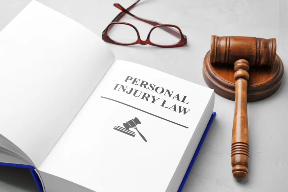 Personal injury law book on table with a gavel and glasses beside it