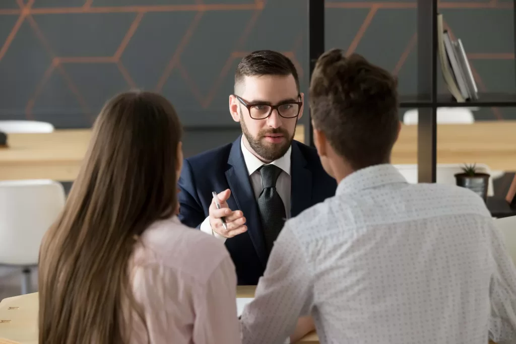 Serious investment broker, financial advisor or bank worker in suit and glasses consulting young couple giving legal advice