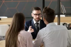 Serious investment broker, financial advisor or bank worker in suit and glasses consulting young couple giving legal advice