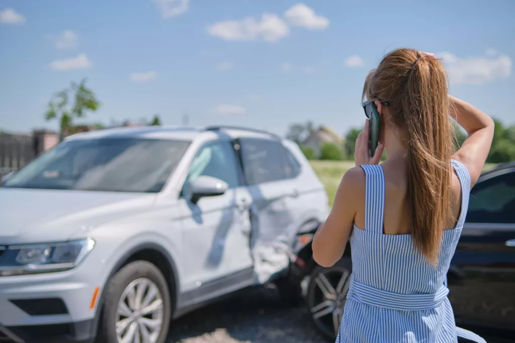 Stressed driver talking on cellphone on roadside near her smashed vehicle calling for emergency service help after car accident.