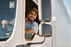 Happy professional truck driver driving his truck and looking at camera