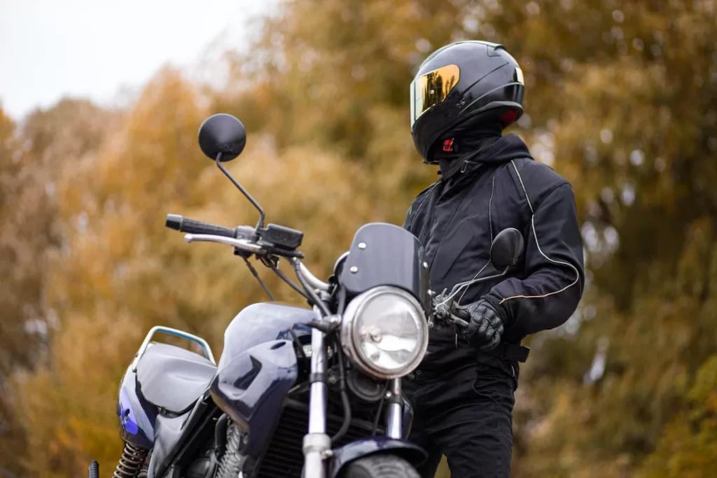 Motorcyclist in a motorcycle jacket and tinted helmet with a classic motorcycle in nature.