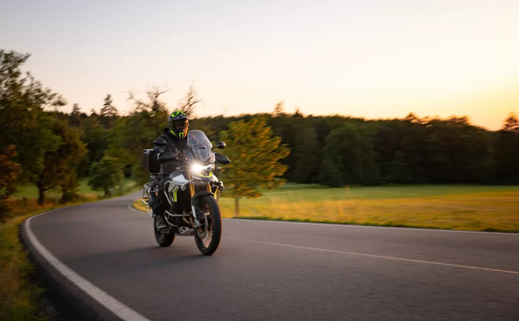 Driver riding motorcycle on empty road during sunset